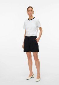 Witte t-shirt met korte mouwen en een zwarte kraag, gecombineerd met stijlvolle zwarte shorts met zakken, net boven de knie en strakke lijnen.