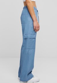 Světle modré nákladní kalhoty s volným střihem, vybavené několika postranními kapsami, stahovací pas s tkaničkou a hladkou džínovou texturou.