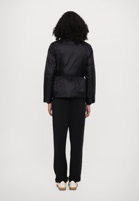 Black puffer jacket with a textured finish, cinched waist, and long sleeves, paired with loose black pants and cream sneakers.