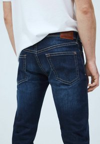 Mörkblå denimjeans med slim fit, med en brun läderetikett, bakfickor och kontrasterande sömmar. Slät yta och klassisk design.