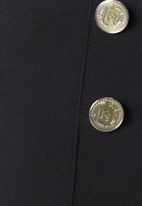 Gros plan sur un tissu noir avec deux boutons argentés brillants gravés d'une couronne de laurier et d'un emblème décoratif.