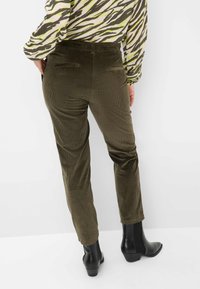 Olivgrüne Cordhosen mit einer glatten Textur. Verfügt über zwei Gesäßtaschen und tapered Beine, kombiniert mit schwarzen Knöchelstiefeln.