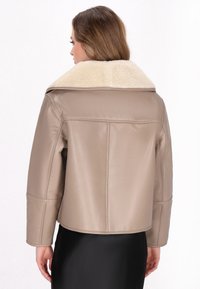 Giacca di pelle beige con un ampio colletto in shearling avorio, spalle strutturate e una vestibilità corta, che mette in mostra una texture liscia e opaca.