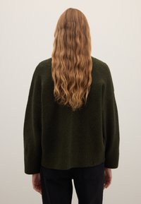 Dunkelgrüner, übergroßer Pullover mit weichem, strukturiertem Strick, mit überschnittenen Schultern und gerippten Bündchen, von hinten gezeigt.