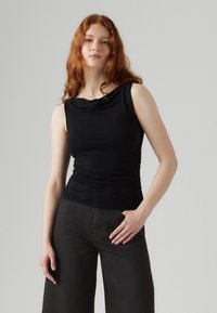 Juoda berankovė palaidinė su draperiuotu iškirptės kraštu, aptemptu liemeniu ir sutrauktu audiniu, derinama su aukšto juosmens tamsiais platėjanti džinsiniais kelnėmis.