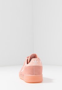 Sneaker in suede rosa con suola in gomma liscia, dotata di un logo bianco sul tallone e un design a striscia laterale sottile.