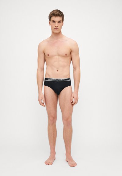 Slips neri con un ampio cinturino elastico che presenta il logo "Emporio Armani". Tessuto liscio, design aderente e stile minimalista.