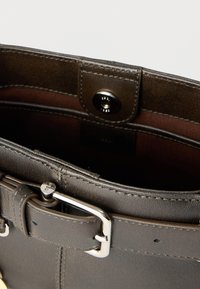 Σκούρα καφέ δερμάτινη τσάντα με ασημένιο αγκράφα και κούμπωμα, που δείχνει λεπτομερείς ραφές και ανοιχτή άποψη του εσωτερικού από πάνω.