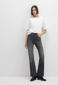 White cotton t-shirt with short sleeves, paired with high-waisted dark grey flared jeans. Black ankle boots complete the outfit.