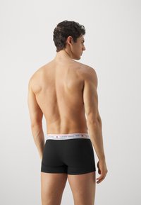 Boxers negros con un cinturón elástico de marca, que presenta "TOMMY JEANS 1985" en letras blancas y rojas. Textura de tela suave.