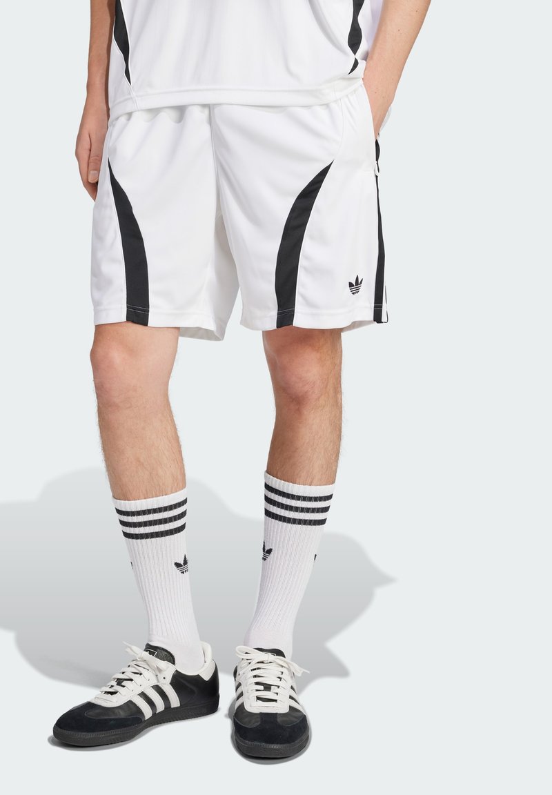 Shorts de sport blancs avec des panneaux latéraux noirs, associés à des chaussettes blanches jusqu'aux genoux avec trois rayures noires et des chaussures de sport noires.