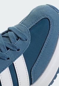 Modré tenisky z kombinácie semišu a textilu, s bielymi pruhmi, textúrovaným povrchom a kontrastnou podrážkou. Šnúrky sú viditeľné.