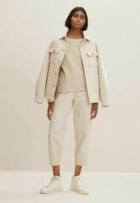 Light beige oversized jacket with two chest pockets, knit beige sweater, and tapered cream pants. Finished with white high-top sneakers.