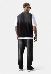 Schwarze Denim-Weste über einem weißen T-Shirt, kombiniert mit grauen, verwaschenen Hosen. Das Outfit zeichnet sich durch kontrastierende Texturen und Steckdetails aus.