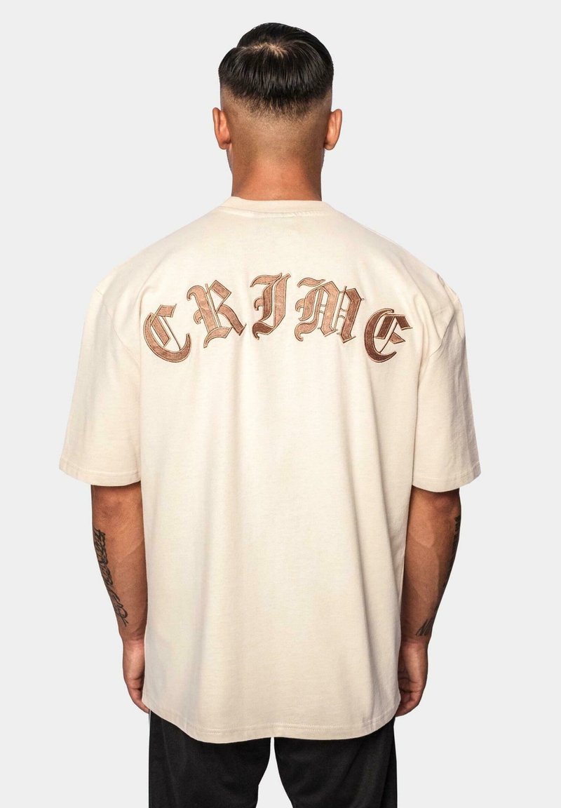 Beige bomulds t-shirt med stort, fedt "CRIME" tekst i stiliseret brun skrift på ryggen. Korte ærmer og afslappet pasform.