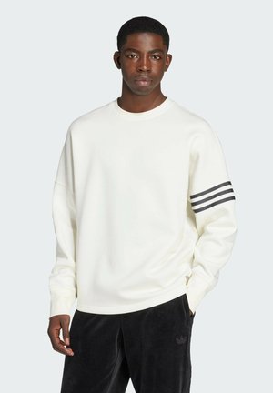 Witte sweatshirt met een ronde hals, drop shoulders en drie zwarte strepen op de linkermouw. Gecombineerd met zwarte velours broek.