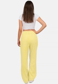 Gelbe, strukturierte weite Hosen mit einem elastischen Bund, kombiniert mit einem weißen Cropped-Top. Ansicht von hinten.