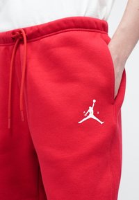 Piros, puha anyagú melegítőnadrág, bal combján fehér Jumpman logóval és állítható derékkal.