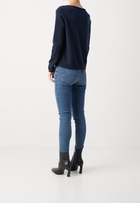 Maglione blu navy con scollatura rotonda, abbinato a jeans blue fitting e stivaletti neri con tacco. Tessuto liscio e design elegante.