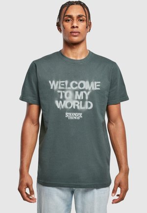 Mørkegrøn bomulds t-shirt med teksten "WELCOME TO MY WORLD" i en falmet spraymalet stil og "STRANGER THINGS" logoet.
