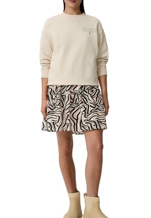 Sudadera crema con texto, combinada con una falda de patrón abstracto en espiral multicolor. El modelo lleva botas de tobillo beige.