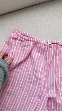 Calças listradas rosa claro com riscas brancas verticais, apresentando uma cintura elástica e um tecido macio e texturado.