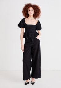 Svart peplum-topp med teksturert stoff, firkantet halsutskjæring og puffede korte ermer, parret med høyt livs svart vide jeans og spisse hæler.
