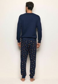 Conjunto de sudadera y pantalones de algodón color azul marino, con un diseño estampado en colores naranja y verde. Puños y bandas en los tobillos ajustados.