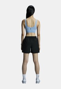 Sportig outfit med en ljusblå sport-bh och svarta shorts. Materialet är slätt; shortsen har en elastisk midja och subtil branding.