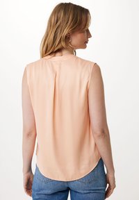 Brzoskwiniowa bezrękawnikowa bluzka z okrągłym dekoltem, miękką teksturą i plisą na plecach. Krągły dół i minimalistyczny design, w połączeniu z niebieskimi dżinsami.