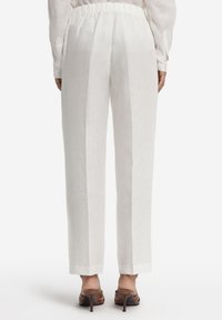 Hvide linnedbukser med en afslappet pasform, der har en bred elastisk talje, lige ben og diskrete sidesømme. Kombineret med brune sandaler med hæl.