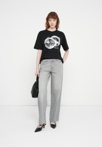 Black t-shirt with a disco ball graphic, paired with light gray straight-leg jeans, black handbag, and black pointed heels.