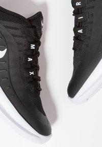 Zapatillas deportivas negras con parte superior de malla, suela de goma y acentos blancos. Presenta el texto "AIR" y superposiciones sintéticas para soporte.