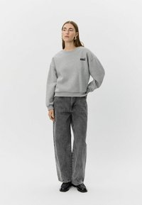 Šedá mikina s nápisom "oui" vytlačeným čiernou farbou, skombinovaná s vysokým pásom sivých džínsov so zúženým strihom. Model má na nohách čierne topánky.