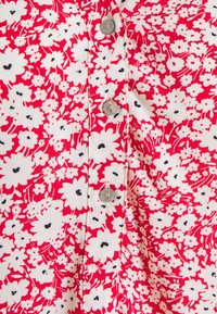 Tessuto floreale rosso con dettagli bianchi e neri, dotato di una fila di bottoni e una texture liscia. Il motivo include piccoli fiori e foglie.