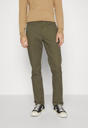 Olive green cotton trousers with a straight fit, featuring belt loops and a button closure, paired with black sneakers.