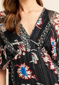 Robe florale multicolore avec un fond noir, design en V, manches transparentes et détails de broderie délicats avec une texture douce.