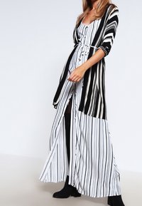 Maxiklänning med svarta och vita vertikala ränder, med en figurnära bodice, ett band i midjan och flödande tyg. Långa ärmar och en delad design.