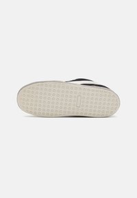 Svartsneaker med en texturerad vit gummisula. Har en slät ovandel med sömmar och en delvis dragkedjestängning.