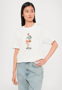 T-shirt en coton blanc avec un imprimé graphique coloré représentant une femme assise, avec des manches rayées. Coupe décontractée et manches courtes.