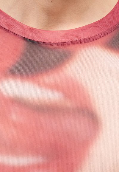 Primer plano de una tela de malla rosa con una impresión borrosa de un rostro abstracto y un escote visible en la parte superior.