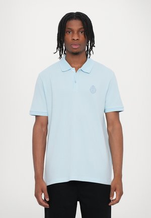 Polo shirt bleu clair avec un col côtelé et une patte de boutonnage, arborant un emblème brodé subtil sur la poitrine et des manches courtes.