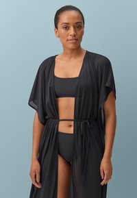 Zwarte lichtgewicht kimono-achtige cover-up met open voorkant, losse mouwen en verstelbare tailleband. Draagt over een zwarte bikini-top en -onderbroek.
