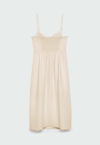 Robe beige clair à fines bretelles, avec un corsage smocké et un tissu texturé. Coupe fluide en ligne A avec un ourlet à hauteur du genou.