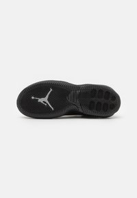Semelle de chaussure de sport en caoutchouc noir avec des motifs de grip texturés, présentant un logo Jumpman gris central et un design courbé au niveau du talon.