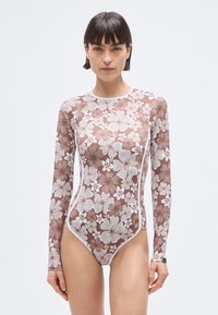 Long-sleeve swimsuit in sheer brown fabric with white floral pattern. Features a round neckline and high-cut leg design.