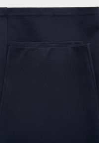 Gros plan sur un tissu bleu marine avec une poche avant rectangulaire avec des coutures visibles et une ceinture plate.