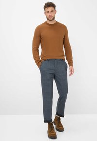 Maglione di lana marrone, pantaloni a quadri grigi e stivali stringati marroni. I pantaloni hanno i risvolti; l'outfit combina texture e colori.