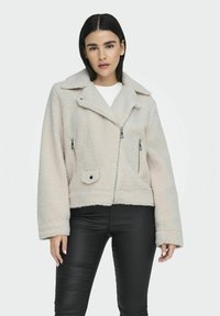 Giacca in shearling foderato di un beige chiaro con colletto a rever, chiusure con zip, due tasche frontali e design crop. Tessuto testurizzato, vestibilità rilassata.
