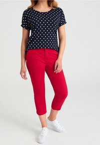 Haut à manches courtes bleu marine à pois, associé à un pantalon court rouge et des baskets blanches. La tenue se caractérise par une coupe décontractée et des couleurs classiques.